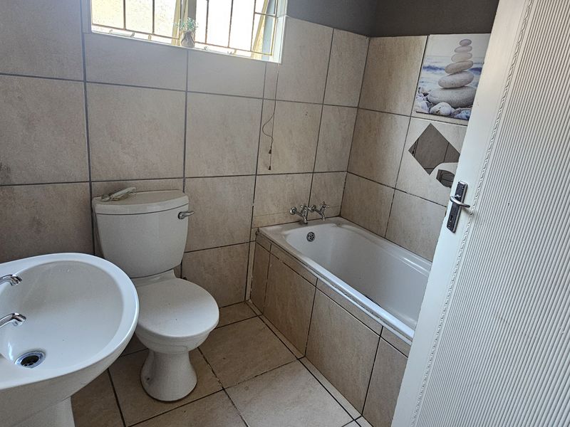 A functional bathroom featuring a pedestal basin, toilet, and a built-in bathtub with neutral wall and floor tiling.