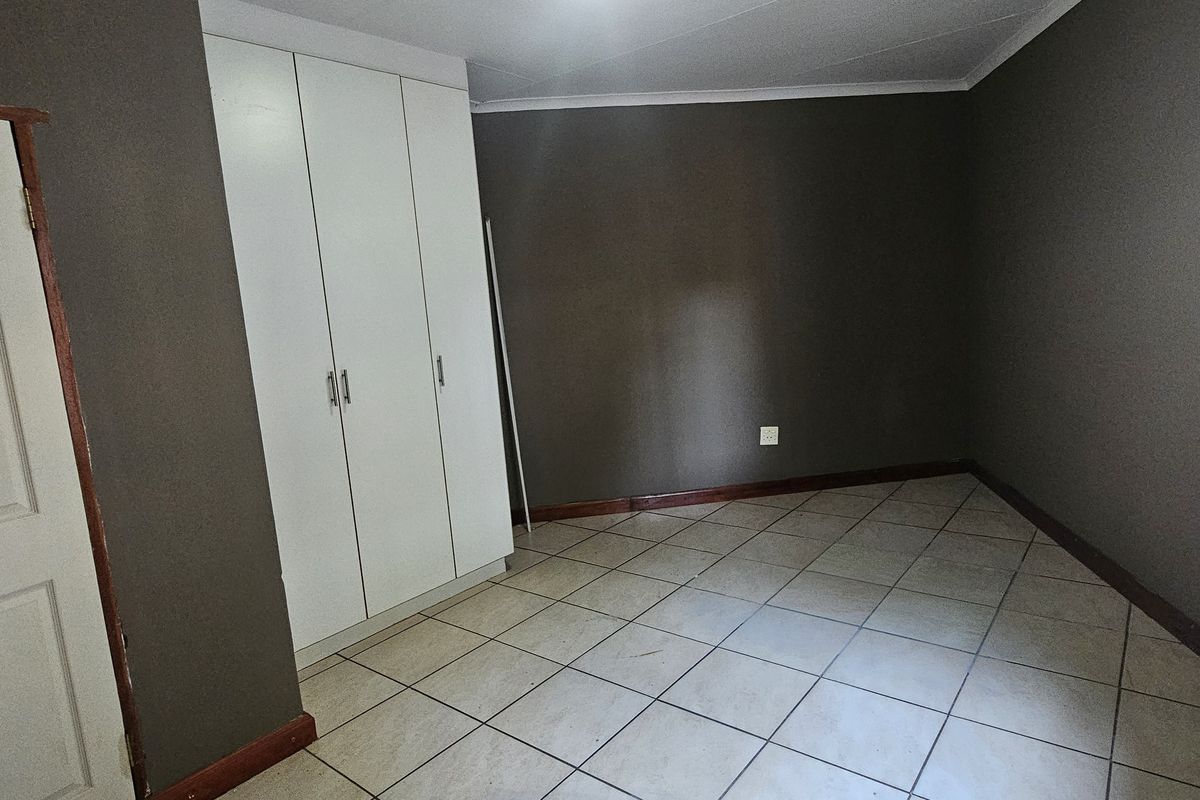 An empty bedroom featuring tiled flooring, dark painted walls, and a built-in wardrobe with security bars on the window.
