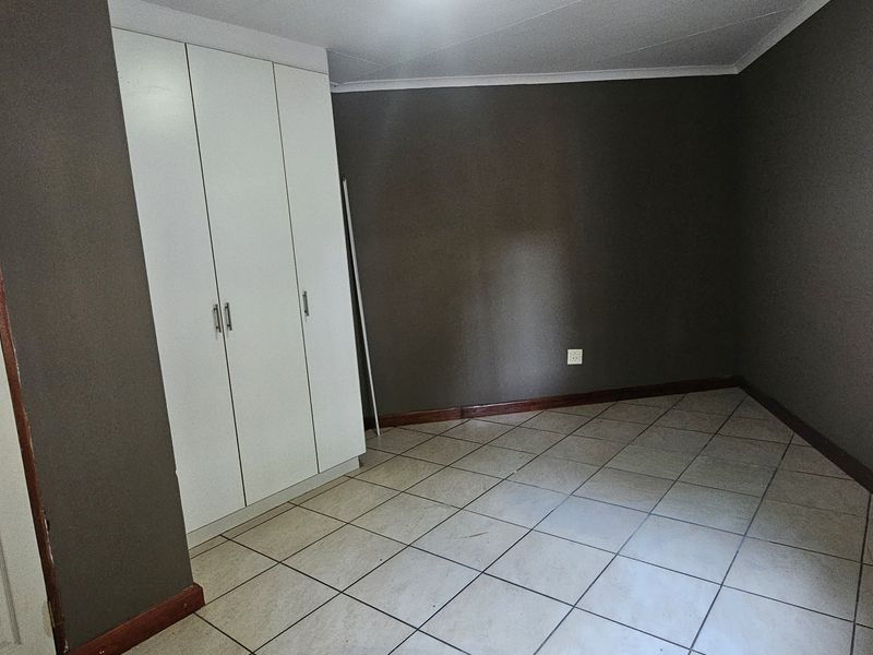 An empty bedroom featuring tiled flooring, dark painted walls, and a built-in wardrobe with security bars on the window.