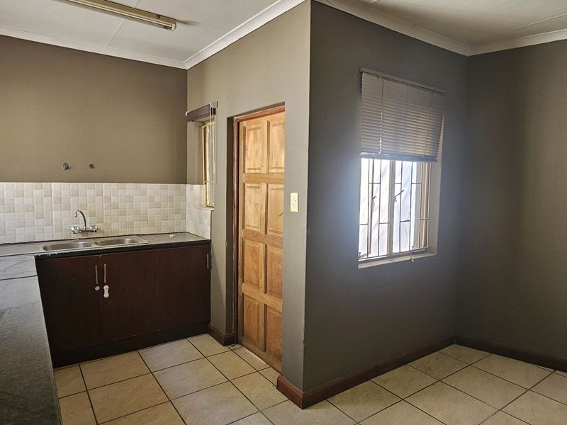 A functional kitchen space featuring dark cabinetry, tiled splashbacks, and tiled flooring, currently vacant and ready for updates.