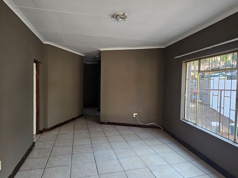 An empty living room featuring tiled flooring, large windows with security bars, and neutral wall tones, offering a blank canvas for interior design.
