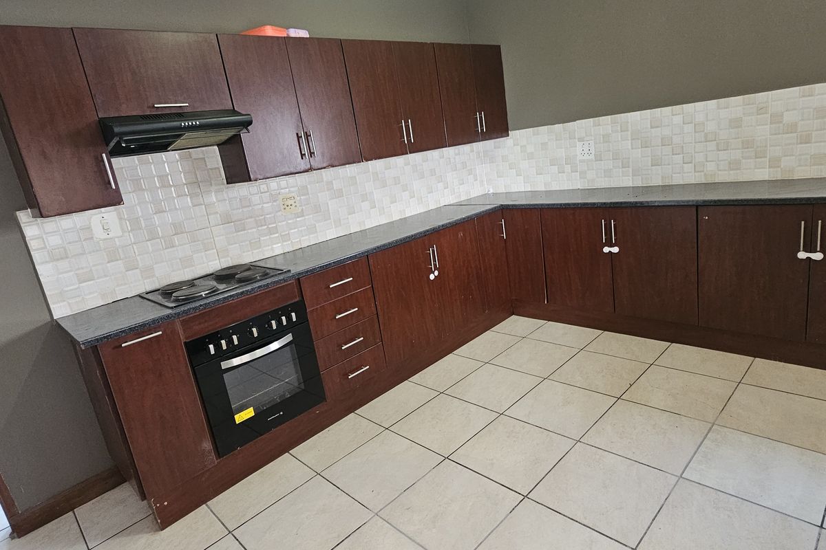 A functional kitchen featuring dark wood-look cabinetry, tiled backsplash, built-in oven, and hob, set against a neutral wall finish with tiled flooring.