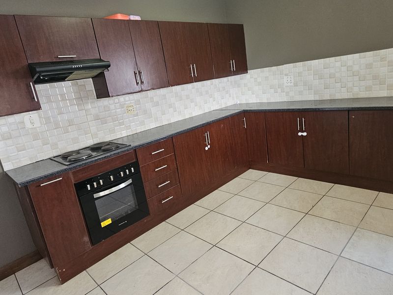 A functional kitchen featuring dark wood-look cabinetry, tiled backsplash, built-in oven, and hob, set against a neutral wall finish with tiled flooring.