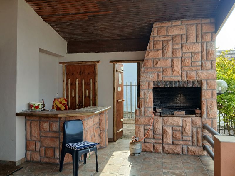 Covered outdoor patio featuring a built-in stone barbecue and matching stone-clad bar counter, providing a rustic space for outdoor entertaining.
