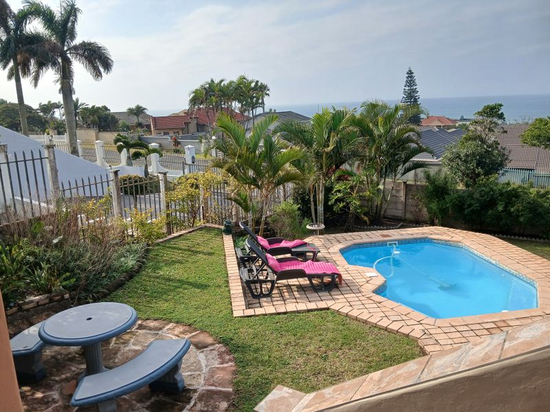 Outdoor pool area featuring a swimming pool, brick paved surround, and a stone patio area with established garden landscaping and ocean views.
