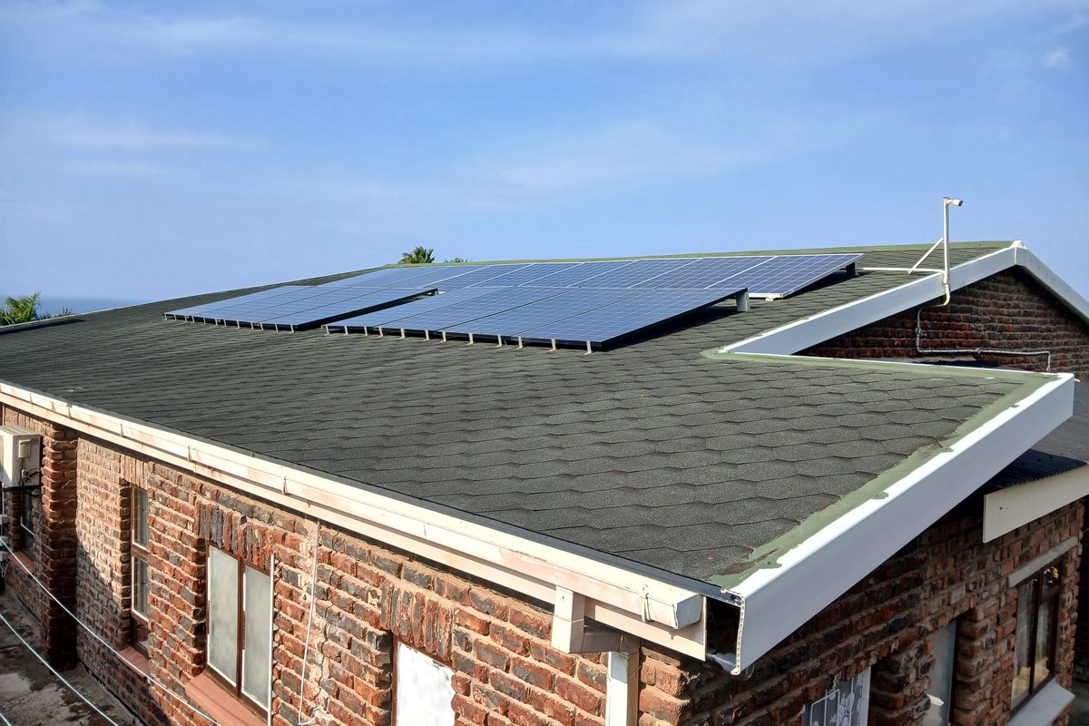 An elevated view of a brick house exterior featuring a roof-mounted solar panel array and standard guttering system.