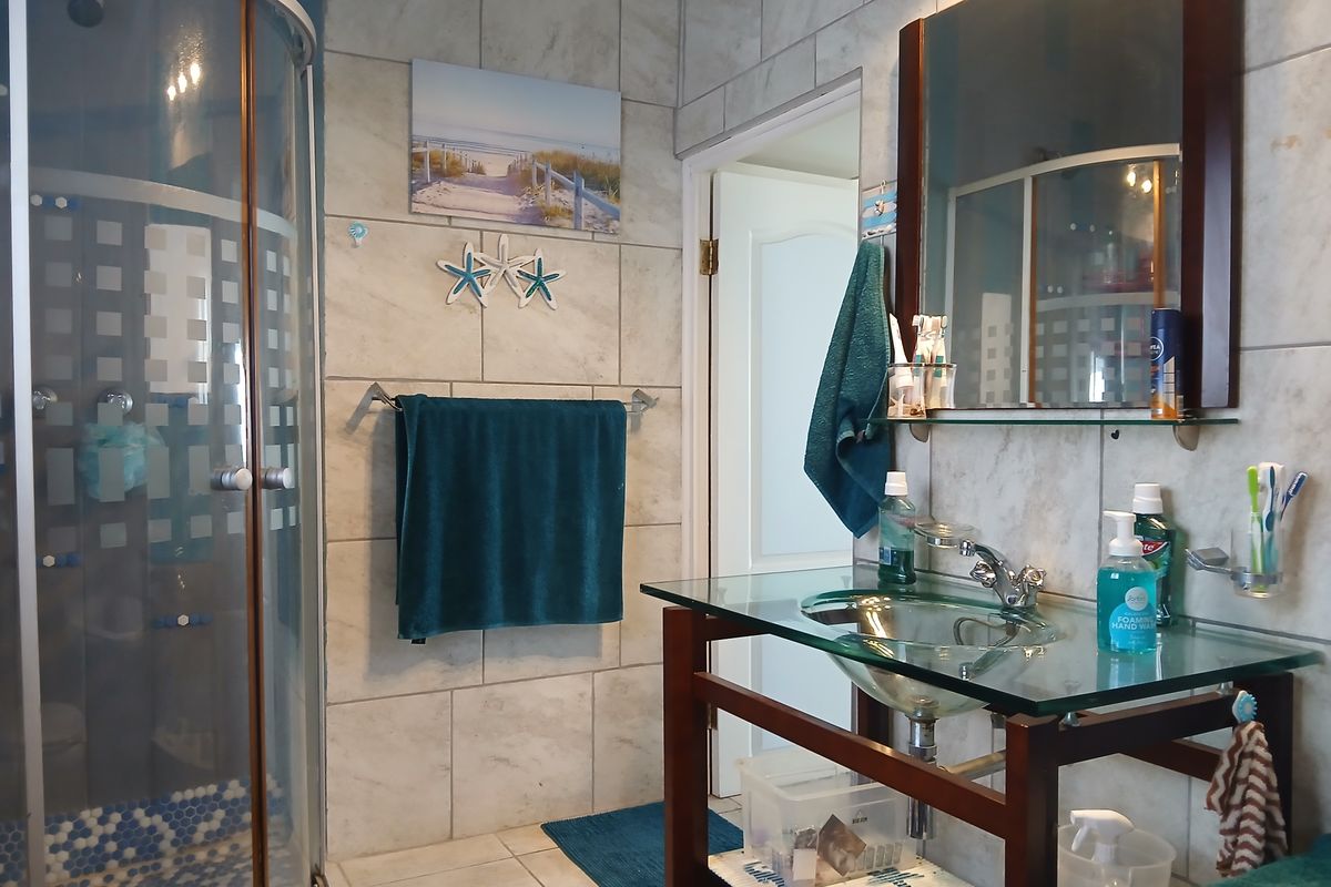 A functional bathroom featuring a curved glass shower enclosure, a modern glass vessel sink with a wooden vanity, and neutral wall tiling.