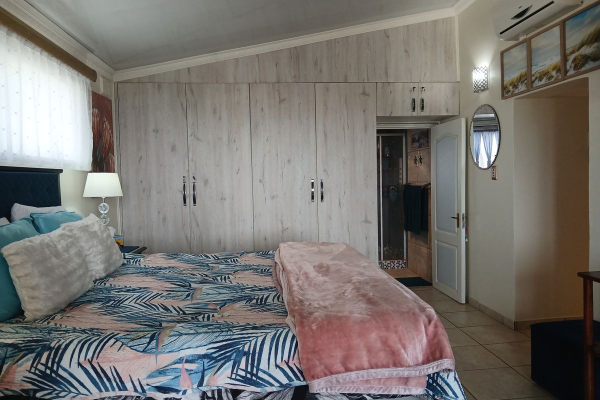 Spacious bedroom featuring extensive built-in cupboards, tiled flooring, and an en-suite bathroom, complemented by a wall-mounted air conditioning unit.
