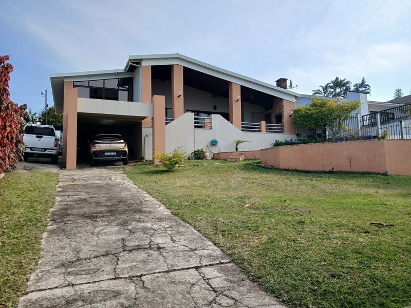 Front elevation of a house featuring a covered carport, concrete driveway, and a raised patio area with brick chimney and retaining wall.