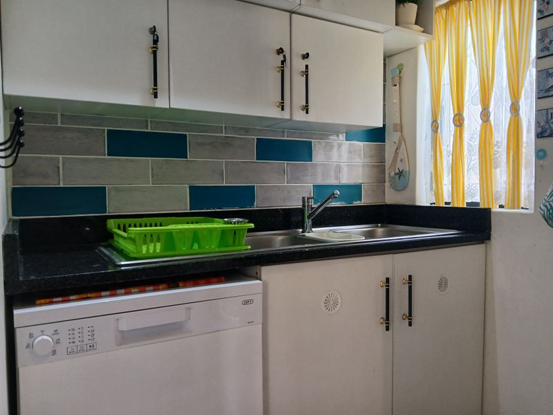 Compact kitchen area featuring white cabinetry, dark granite countertops, a stainless steel sink, and a modern tiled backsplash.