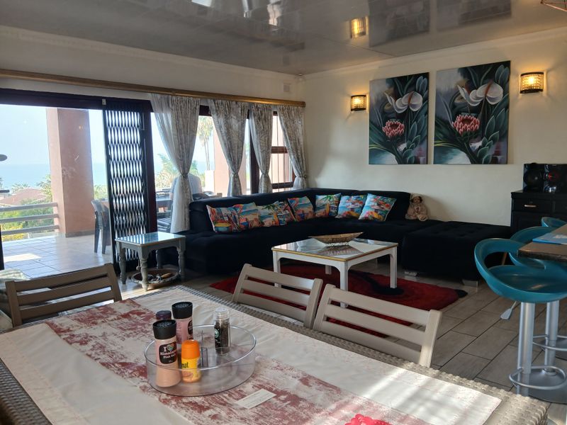 Spacious open-plan living and dining area featuring tiled floors, modern wall lighting, and large sliding doors opening to an outdoor patio with sea views.