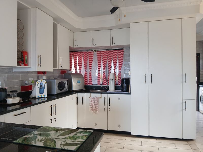 A well-maintained kitchen featuring white cabinetry, dark granite countertops, subway tile backsplash, and tiled flooring with integrated storage solutions.