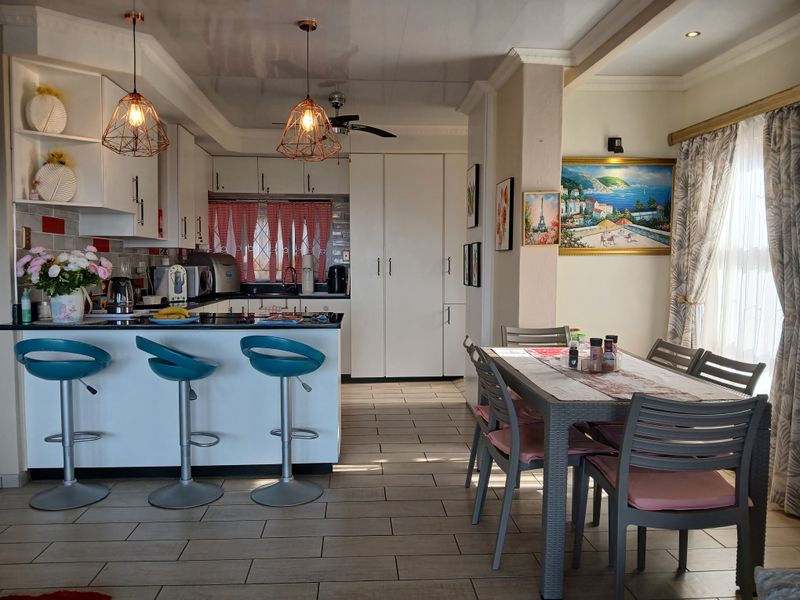 An open-plan kitchen and dining area featuring modern cabinetry, a breakfast bar, tiled flooring, and stylish pendant lighting.