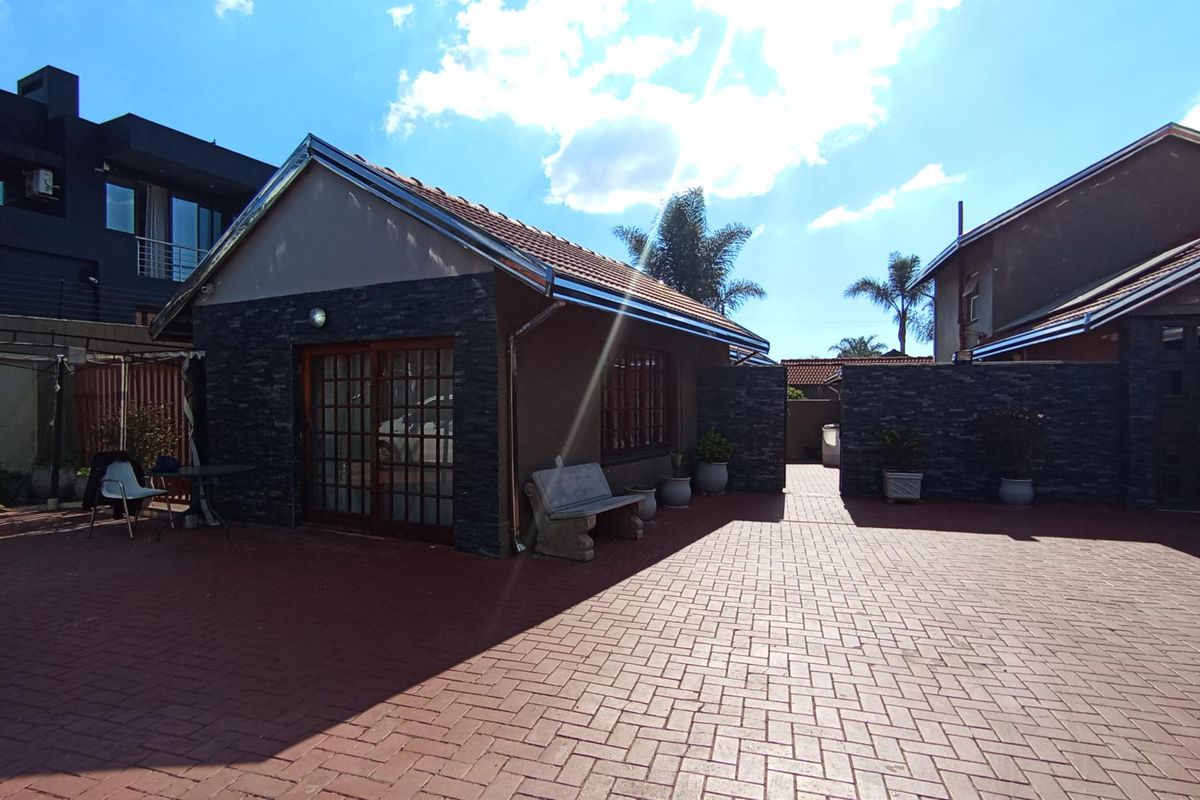 A well-maintained rear exterior area featuring paved surfacing, stone-clad feature walls, and sliding door access to the main structure.