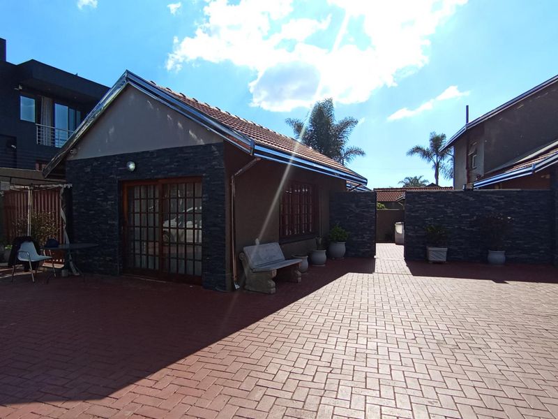 A well-maintained rear exterior area featuring paved surfacing, stone-clad feature walls, and sliding door access to the main structure.
