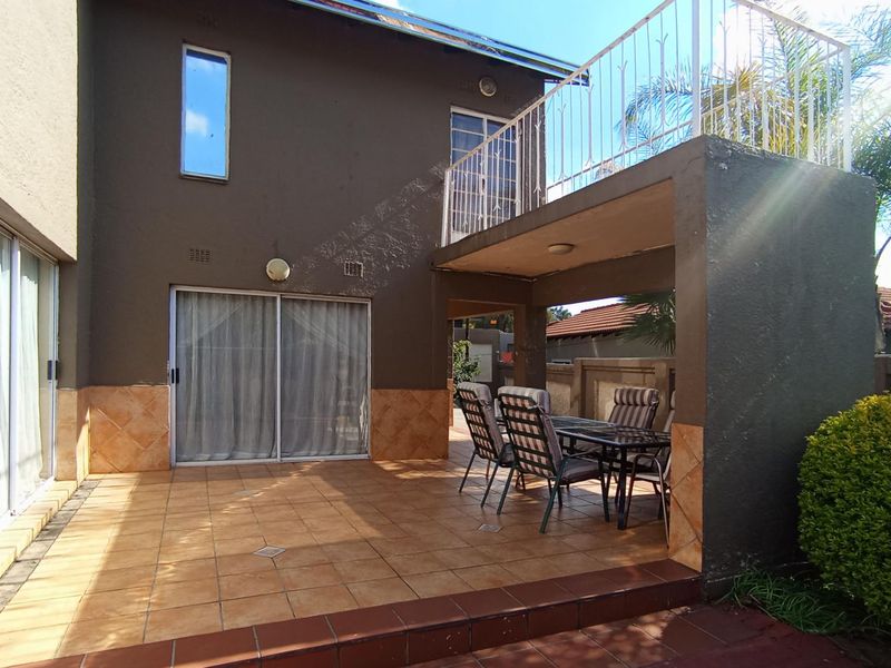 A covered patio area featuring tiled flooring, sliding glass doors, and an upper-level balcony with metal railings, suitable for outdoor dining and relaxation.