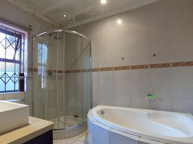 A bathroom featuring a corner bathtub, a curved glass shower enclosure, and tiled finishes. The ceiling shows signs of water damage.