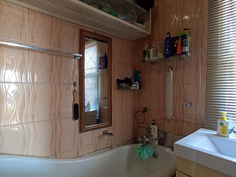 A functional bathroom featuring a bathtub, vanity basin, and dated wall tiling, offering potential for a modern renovation.