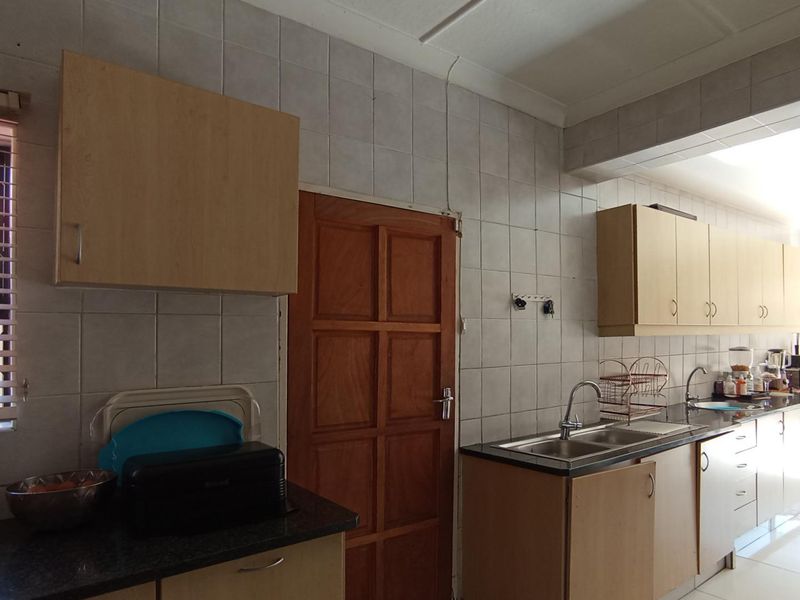 A dated kitchen featuring laminate cabinetry, tiled splashbacks, and a double bowl stainless steel sink, requiring cosmetic updates to improve functionality and aesthetic appeal.