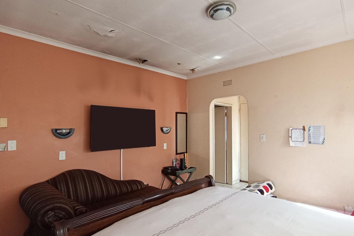 A bedroom featuring an arched doorway and wall-mounted lighting, currently showing significant signs of ceiling water damage and plaster deterioration.