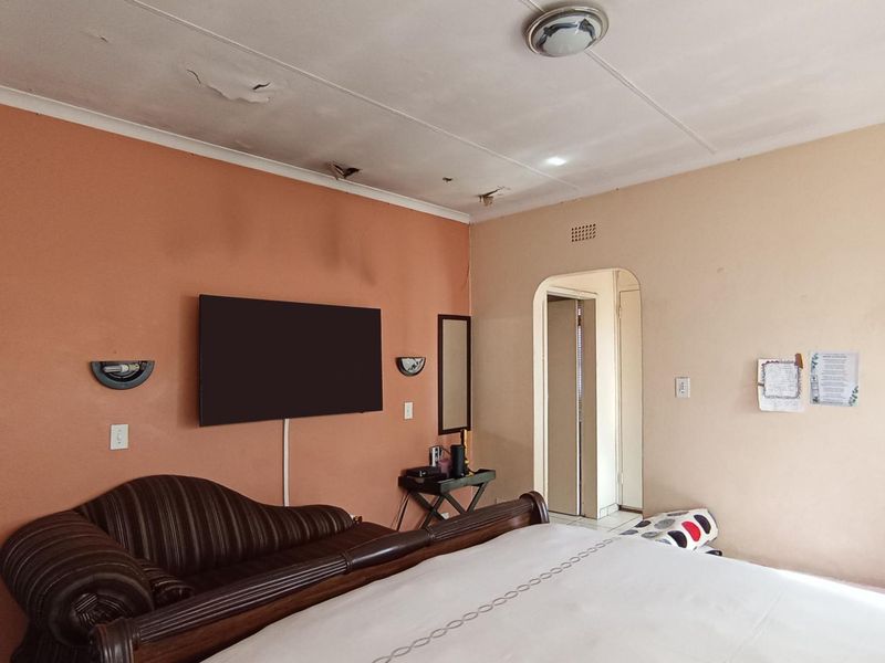 A bedroom featuring an arched doorway and wall-mounted lighting, currently showing significant signs of ceiling water damage and plaster deterioration.