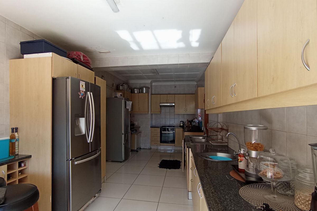 A functional galley-style kitchen featuring light wood cabinetry, granite countertops, tiled flooring, and integrated stainless steel appliances.