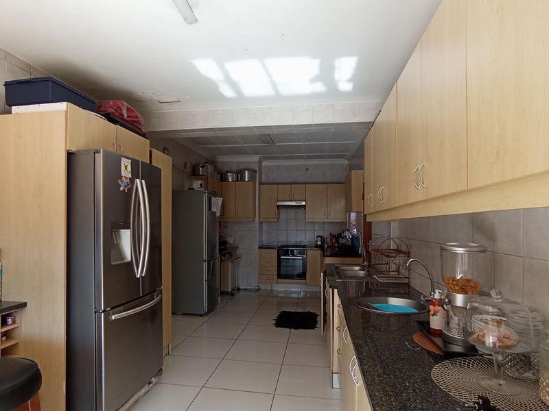A functional galley-style kitchen featuring light wood cabinetry, granite countertops, tiled flooring, and integrated stainless steel appliances.
