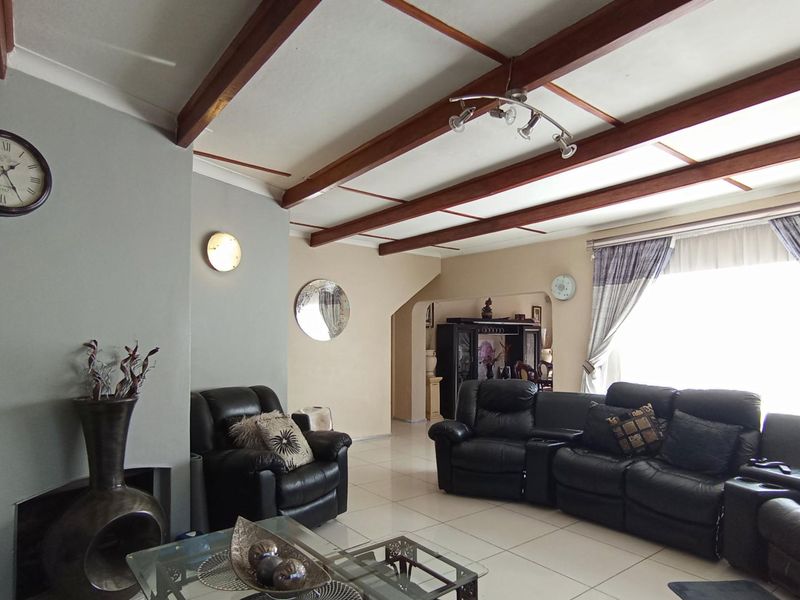 Spacious living room featuring exposed timber ceiling beams, tiled flooring, and a recessed fireplace, offering a comfortable and characterful living space.
