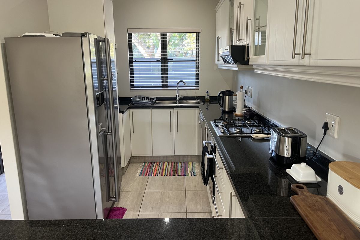 A functional kitchen featuring granite countertops, gas hob, extractor fan, double sink, and ample built-in cabinetry with tiled flooring.