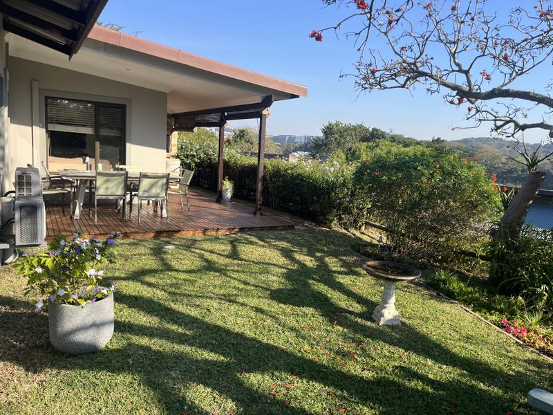 A well-maintained rear garden featuring a timber deck patio, established landscaping, and scenic views, providing an ideal space for outdoor relaxation.