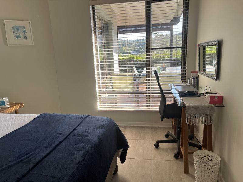 A well-lit bedroom featuring tiled flooring and a large window with venetian blinds, providing direct access to an outdoor patio area.
