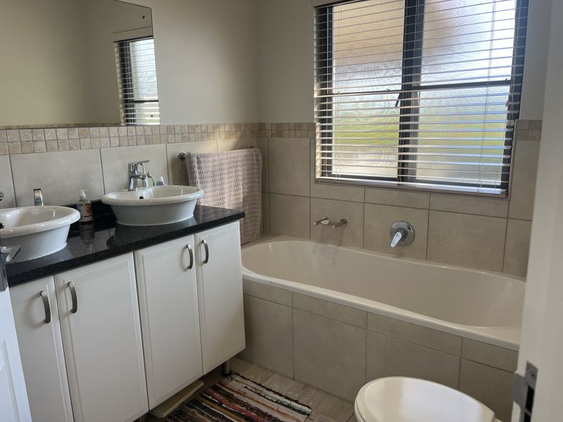 A well-maintained bathroom featuring a double vanity with granite countertops, a built-in bathtub, and neutral wall tiling.