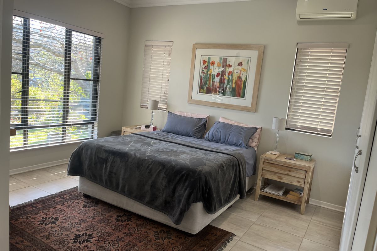 Spacious bedroom featuring tiled flooring, split-system air conditioning, ceiling fan, and large windows with fitted venetian blinds.