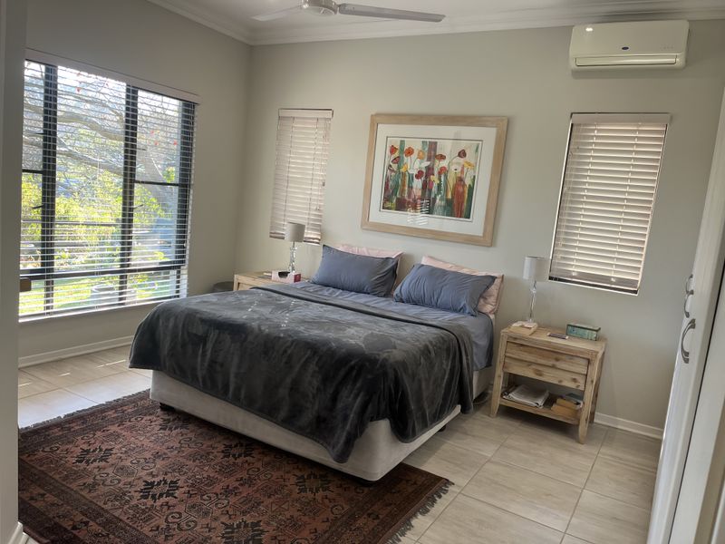 Spacious bedroom featuring tiled flooring, split-system air conditioning, ceiling fan, and large windows with fitted venetian blinds.