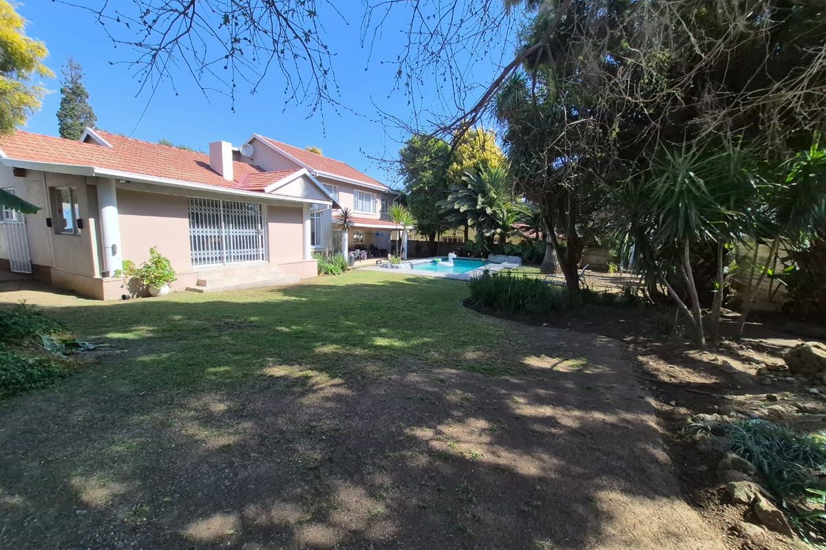 Rear view of the property featuring a swimming pool, established garden, and a tiled roof structure with security gates.