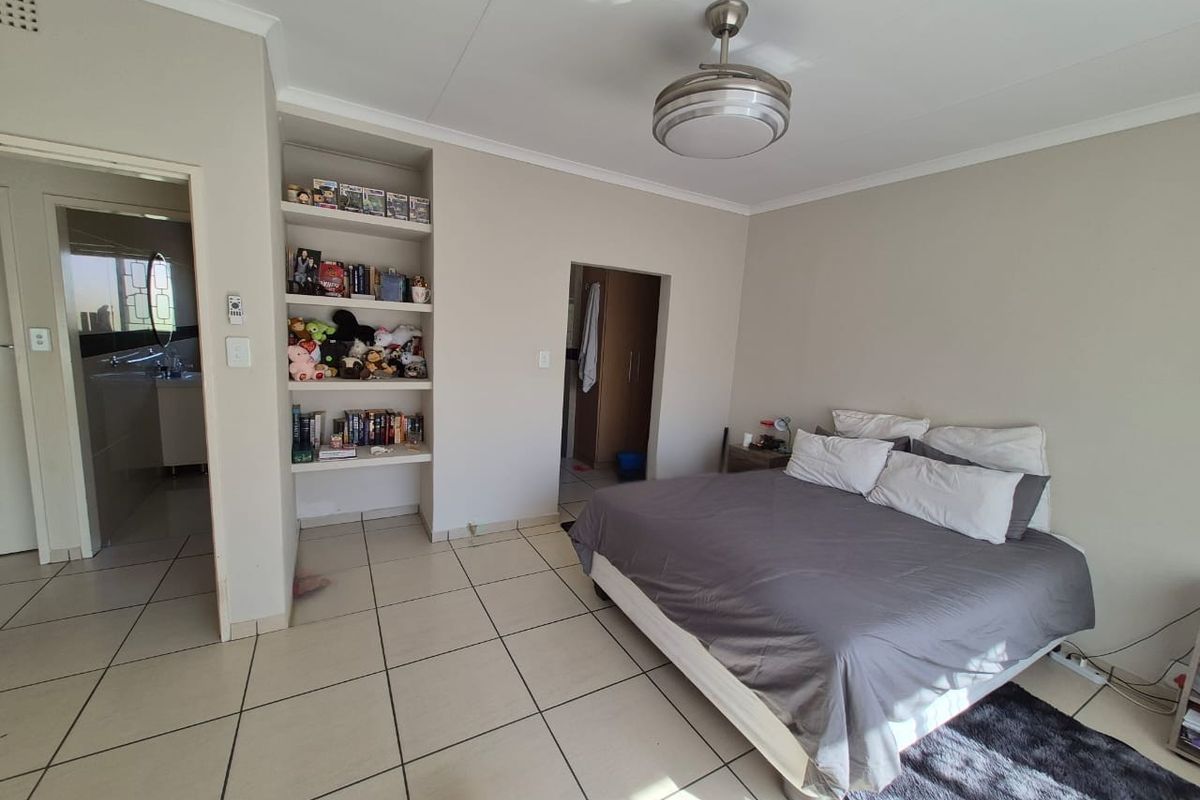 Spacious bedroom featuring neutral tiled flooring, a ceiling fan, and convenient built-in shelving, with direct access to an en-suite bathroom.