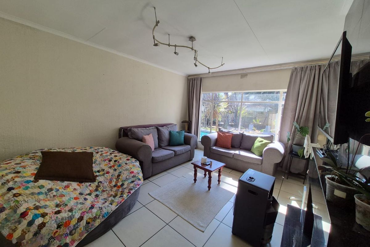 A spacious living room featuring tiled flooring, track lighting, and a large window providing natural light and views of the garden.