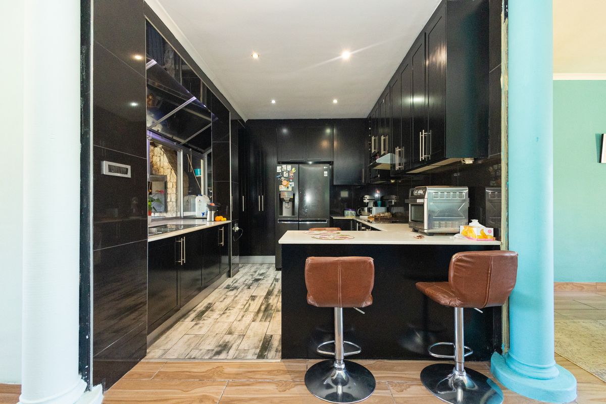 Modern kitchen featuring sleek black cabinetry, stone countertops, and a breakfast bar, with recessed lighting and a contemporary tiled floor finish.