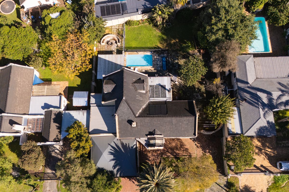 Aerial view of the property showcasing the main dwelling, tiled roof with solar panels, swimming pool, and surrounding landscaped garden areas.