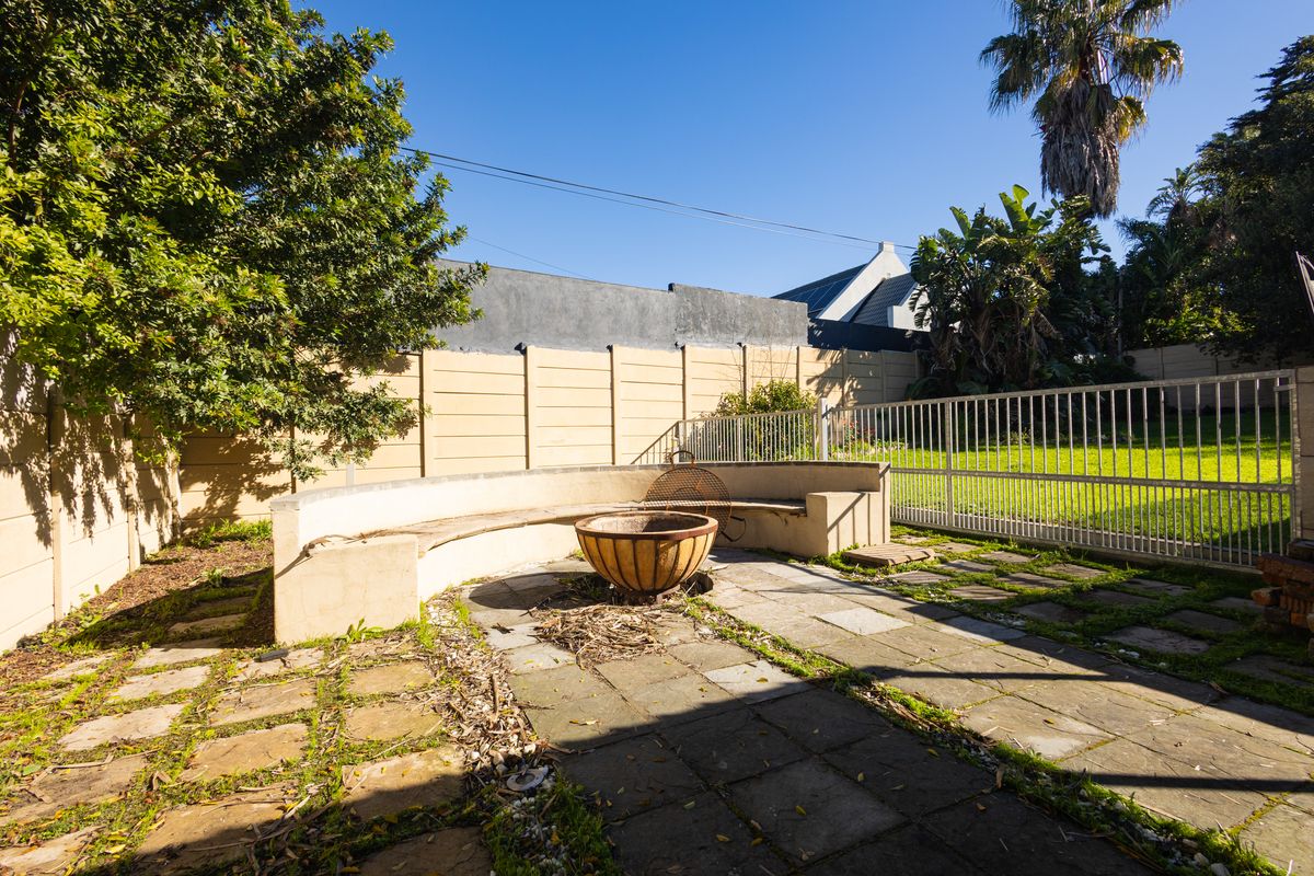 Rear garden area featuring a paved patio with a built-in concrete bench and fire pit, enclosed by boundary walls and security fencing.