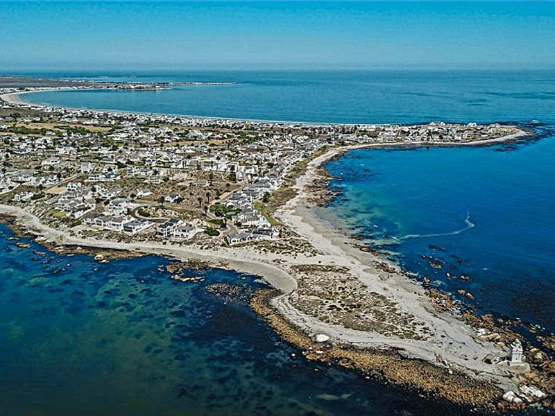 An aerial view of the coastal residential area, showcasing the expansive oceanfront, surrounding landscape, and local lighthouse.