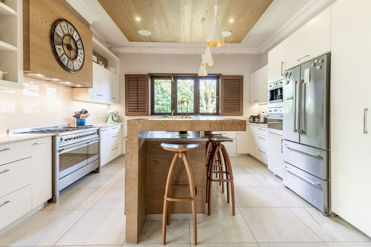 Modern kitchen featuring a central timber-accented island, high-end gas stove, built-in oven, and elegant timber ceiling detailing with integrated lighting.