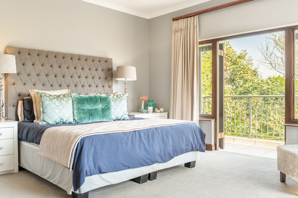 Spacious bedroom featuring neutral carpeting, elegant wall finishes, and direct access to a private balcony with scenic garden views.