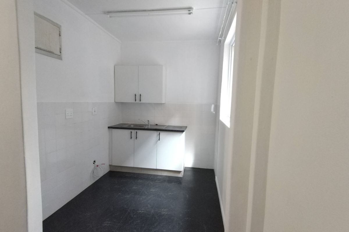 A compact, empty kitchen featuring white built-in cabinetry, a sink, and tiled splashbacks, providing a clean and functional space.