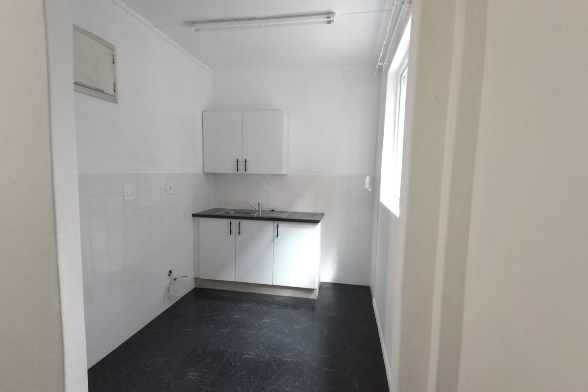 A functional, empty laundry room featuring built-in white cabinetry, a sink, tiled splashbacks, and durable dark vinyl flooring.