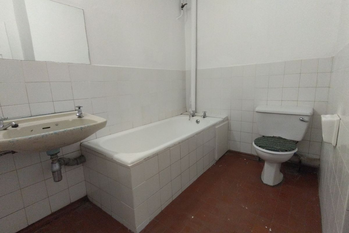 A dated bathroom featuring a bathtub, pedestal sink, and toilet with original wall tiling and exposed plumbing, requiring modernization and cosmetic updates.
