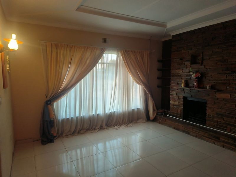 A spacious living room featuring a prominent stone-clad fireplace, tiled flooring, and recessed ceiling detail, offering a neutral canvas for interior design.