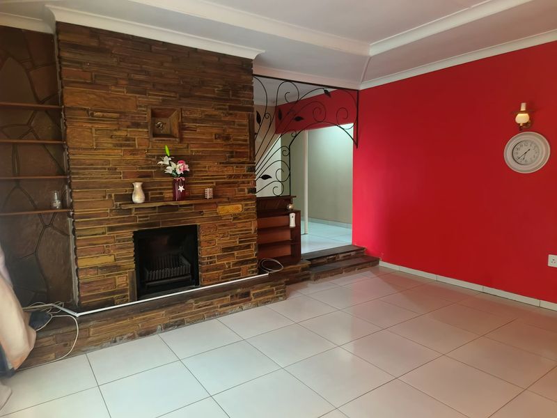 Spacious living room featuring a prominent stone fireplace, decorative wrought iron divider, and neutral tiled flooring, offering a versatile layout for modern updates.