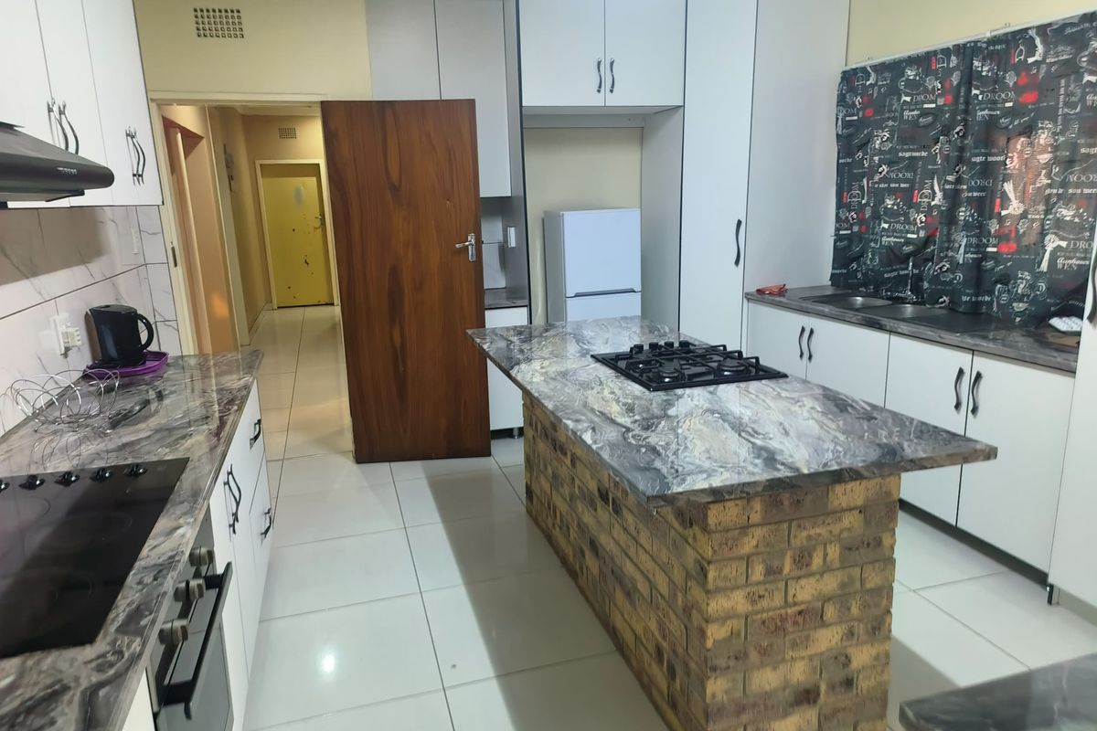 A functional kitchen featuring a brick-base island with a gas hob, marble-effect countertops, white cabinetry, and tiled flooring.