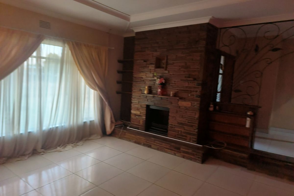 Spacious living room featuring a prominent stone-clad fireplace, tiled flooring, and decorative wrought iron detailing, offering a solid foundation for modern updates.